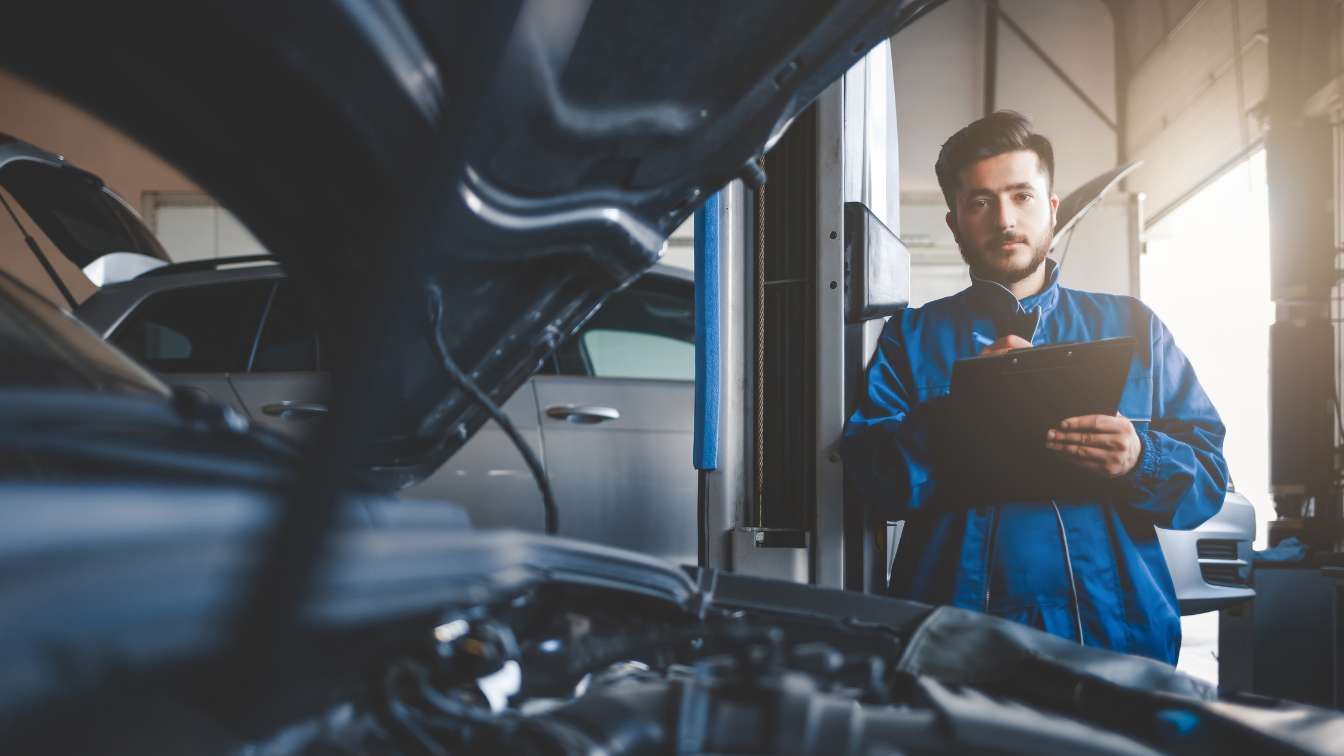 Mechanic beside an open vehicle hood in a repair shop