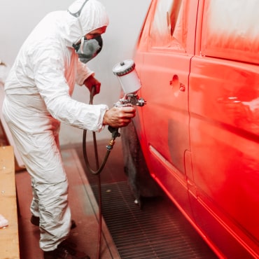 Technician in protective equipment spray-painting a vehicle panel