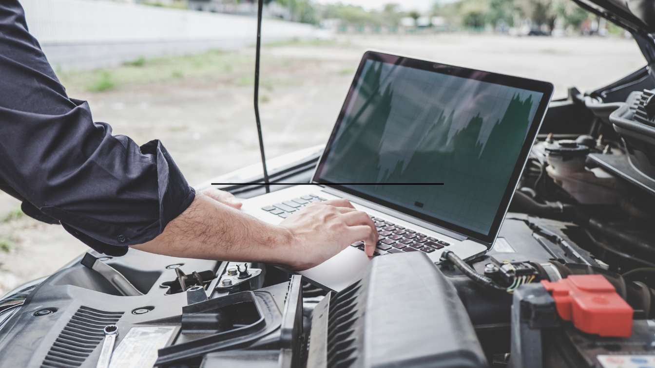 Technician using a laptop while inspecting a vehicle engine during diagnostic work