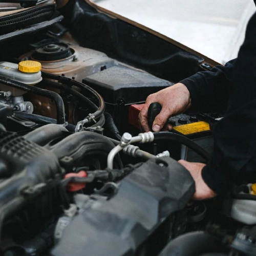 A person is working on a car engine in Auto Repair Surrey, skillfully using a tool to adjust or repair a component under the hood.