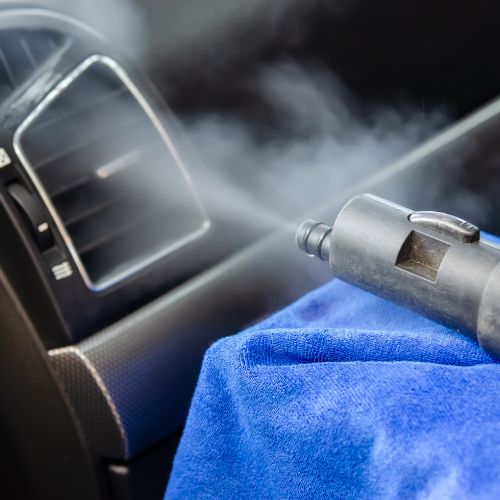 Steam cleaning a car interior with a blue cloth nearby.
