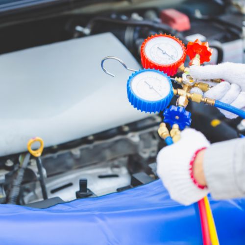 Person checking car engine with pressure gauges, wearing gloves.