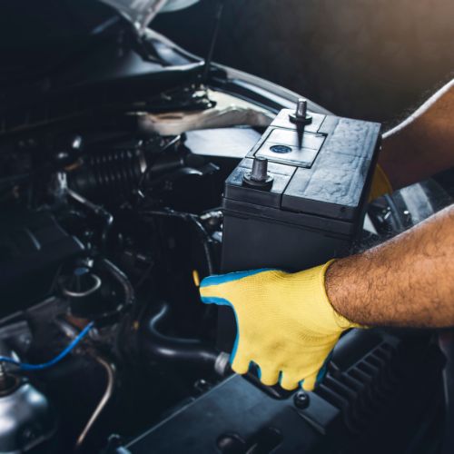 Person wearing yellow gloves installing a car battery under the hood.