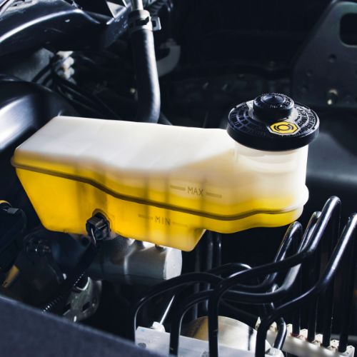Close-up of a car's brake fluid reservoir under the hood, showing fluid level markings and a black cap with a yellow symbol.