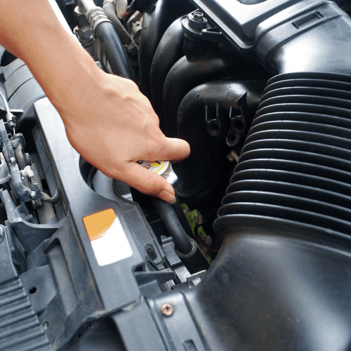 A hand opening a car's radiator cap in the engine bay.