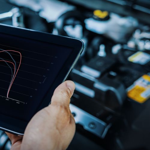 A hand holds a tablet displaying a performance graph in front of a car engine.