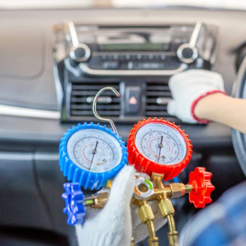 A person adjusts a car's air conditioning controls while holding HVAC manifold gauges.