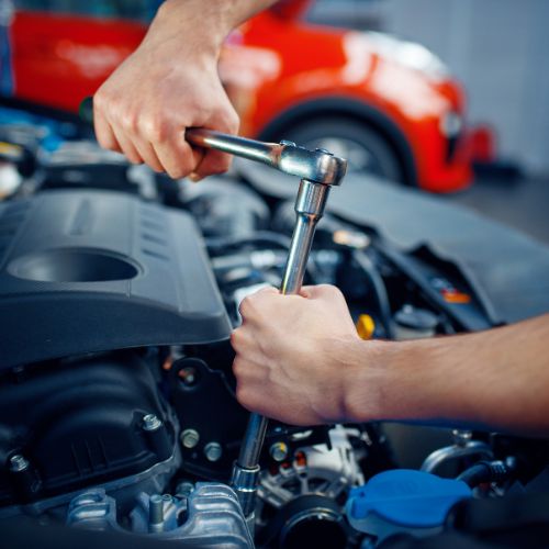 A person uses a socket wrench to adjust a component in a car engine bay.