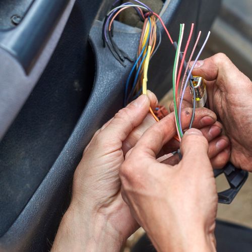 Hands holding and working with exposed wires inside a vehicle.