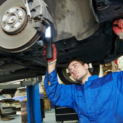 Mechanic in blue coveralls inspects the underside of a vehicle on a lift in a garage.