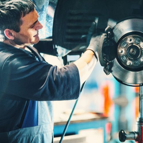 Mechanic inspects and works on a car's brake system in a garage.
